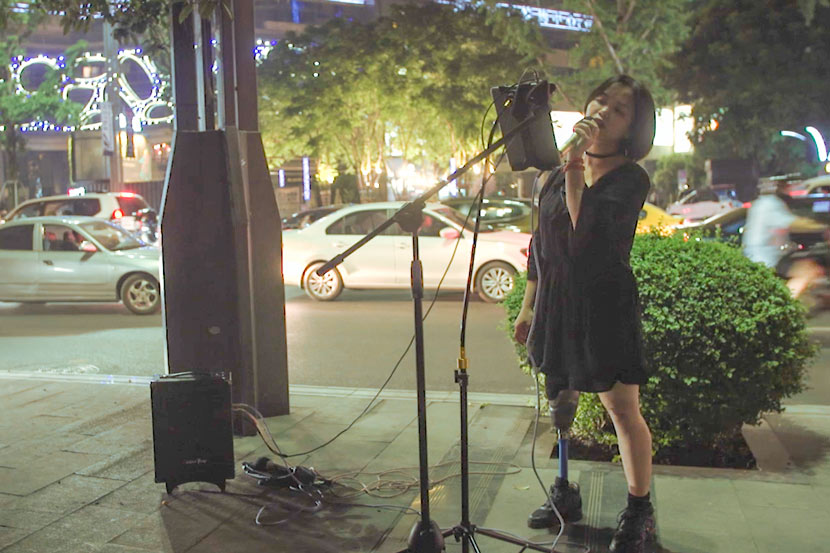 Xie Renci sings into a microphone on a sidewalk in Chongqing, May 20, 2017. Lü Xiao/Sixth Tone