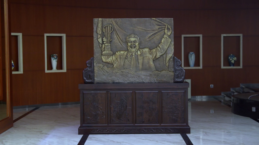 A screenshot showing a relief sculpture of Fuyao CEO Cao Dewang. From Douban. Cao is depicted holding an entrepreneurship award and the Chinese flag.