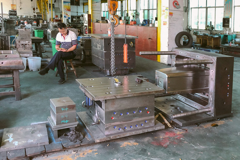 A man sits behind a plastic trash can molding machine at Zhejiang Jiuyuan Plastic Co’s production facility in Taizhou, Zhejiang province, July 29, 2019. Fu Danni/Sixth Tone
