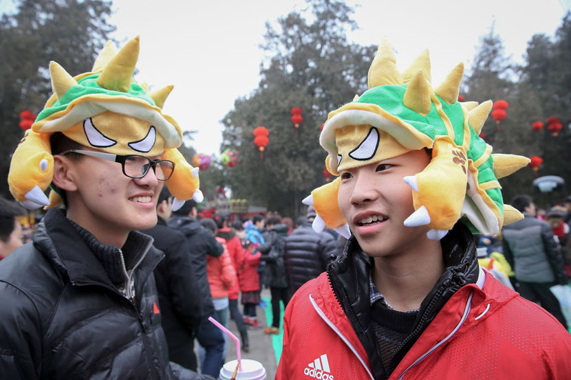 Two young men wear hats styled as Armordillo, a character from the game “League of Legends,” during a temple fair in Beijing, Feb. 1, 2014. Chen Xiaogen/VCG