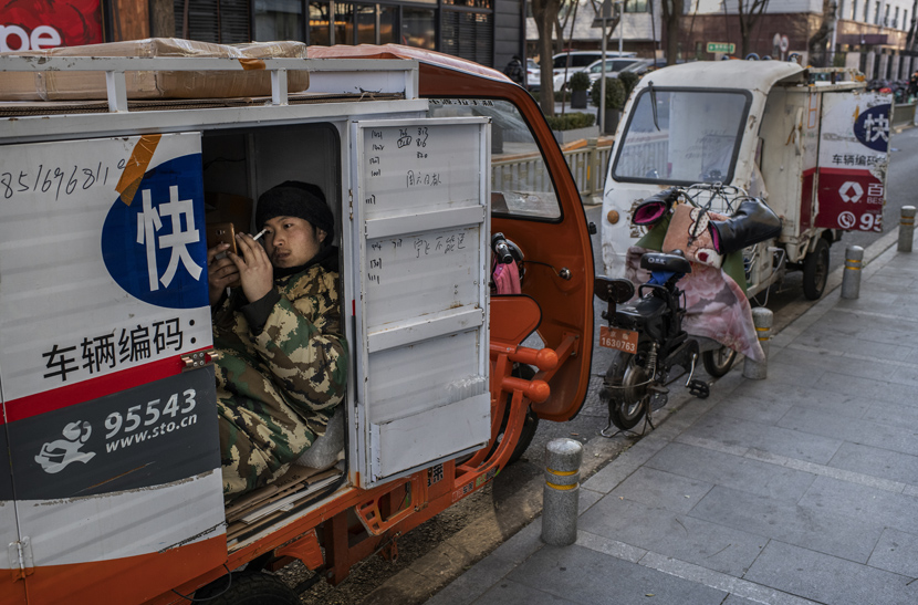 A courier driver watches a video on his cell phone while taking a break in a shopping district in Beijing, Dec. 10, 2019.
