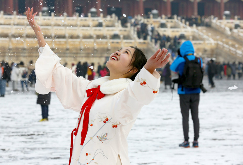A woman throws snow into the air while posing for photos at the Palace Museum in Beijing, Nov. 30, 2019. VCG