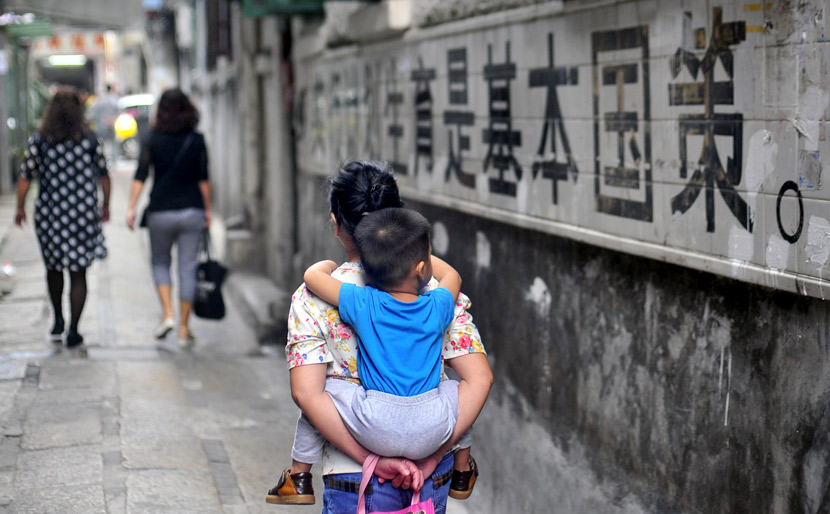 A woman holding a child walks past a slogan for family planning in Guangzhou, Guangdong province, Nov. 6, 2015. Tuchong
