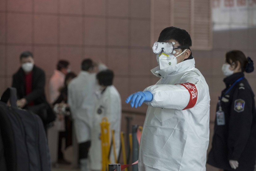 A worker in a protective suit directs passengers at Shanghai Railway Station in Shanghai, Jan. 31, 2020. Yi Chuan for Sixth Tone