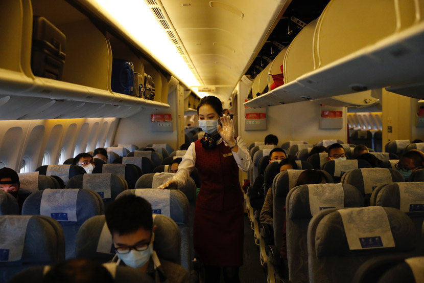 A flight attendant wearing a face mask assists passengers during a flight from Chongqing to Beijing, Jan. 29, 2020. Jiang Wenjie for Sixth Tone