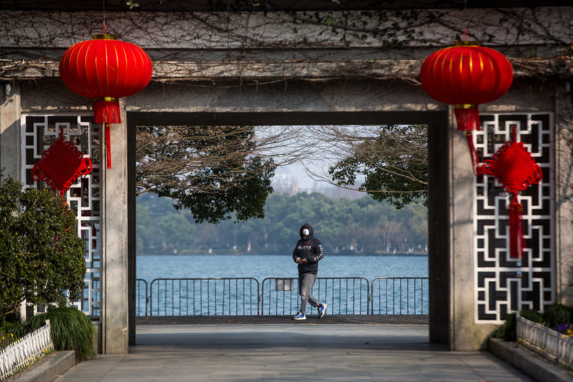 A tourist wearing a mask walks along the West Lake in Hangzhou, Zhejiang province, Jan. 30, 2020. Chen Zhongqiu for Sixth Tone