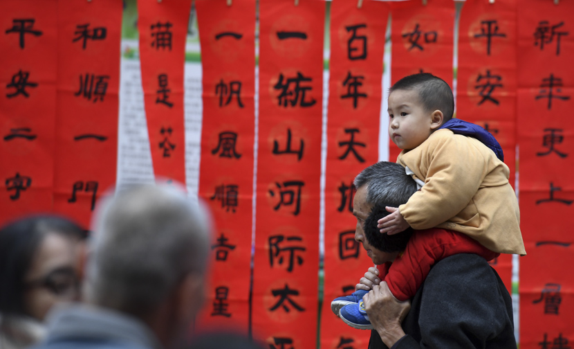 A boy perches on his grandfather’s shoulders in front of spring couplets in Nanning, Guangxi Zhuang Autonomous Region, Jan. 18, 2020. Lu Boan/Xinhua