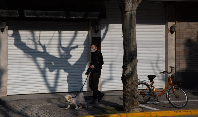 A man walks his dog past shuttered businesses in Shanghai, Feb. 12, 2020. Shi Yangkun/Sixth Tone