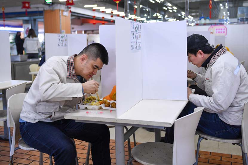 Workers eat lunch at the cafeteria of Jinhe Transportation Equipment Co. Ltd. in Changchun, Jilin province, Feb. 17, 2020. Some company canteens are using partitions to keep staff separated while eating and reduce the risk of cross-infection. Xinhua