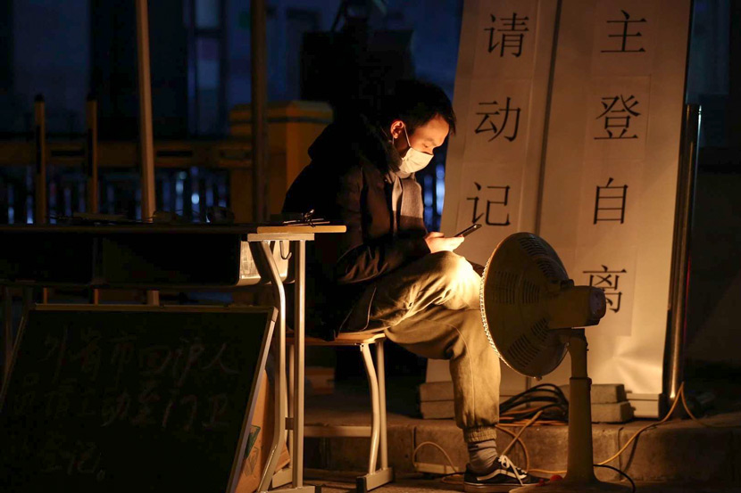 A man in charge of registering residents as they return to Shanghai after the Lunar New Year holiday checks his smartphone at the entrance of an urban residential community, Feb. 8, 2020. Zhu Weihui for Sixth Tone