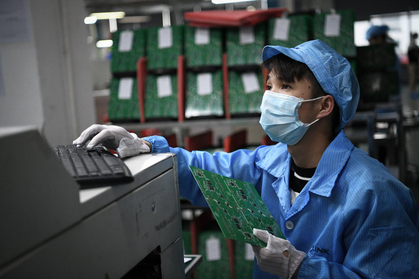 A worker wearing a mask checks a circuit board at a workshop in Shenzhen, Guangdong province, March 12, 2020. Liang Xu/Xinhua