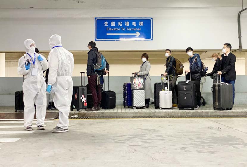 New arrivals from abroad are guided by medical workers to take a shuttle bus at Shanghai Pudong International Airport, March 19, 2020. Xinhua