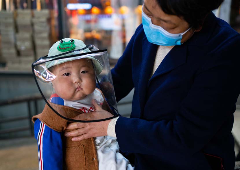 A woman adjusts a child’s mask in Chongqing, April 2, 2020. Liu Song for Sixth Tone