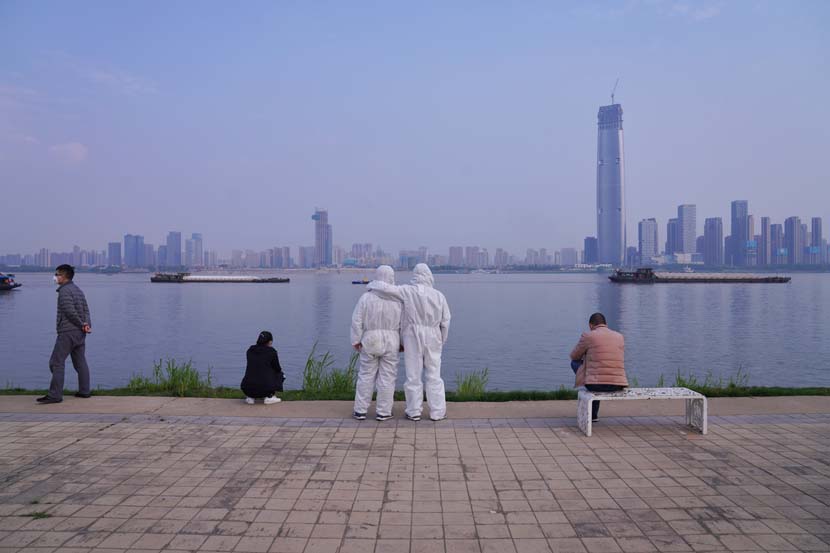 Two men in protective gear look out at the river on Tomb-Sweeping Day in Wuhan, Hubei province, April 4, 2020. Mai Quan for Sixth Tone