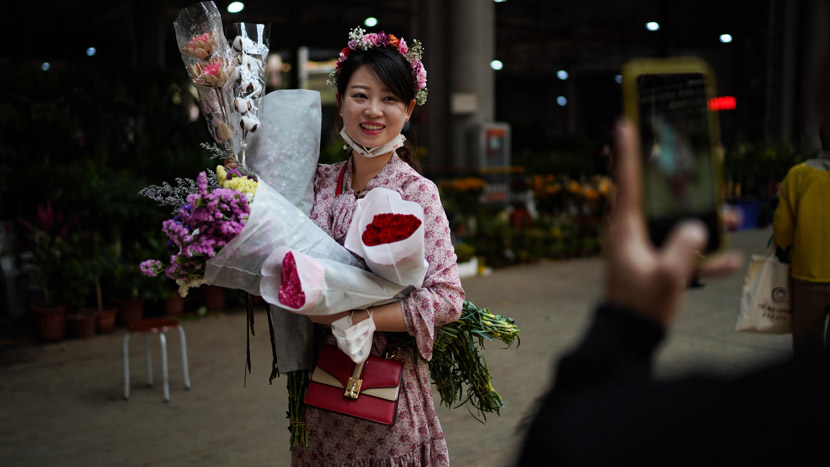 A woman poses for a photo after buying several bouquets of flowers at a market in Kunming, Yunnan province, April 6, 2020. Kang Ping/CNS/People Visual