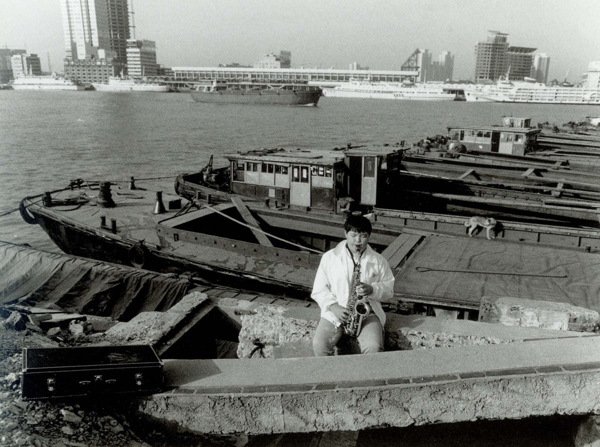 A man plays saxophone on a dock in Shanghai, 1999. Courtesy of Wu Jianping