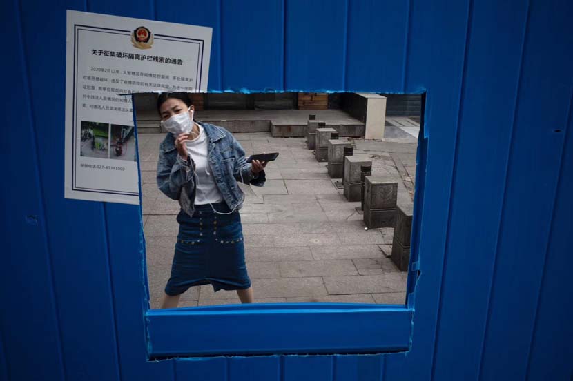 A woman looks through a hole in the wall as she waits for a delivery in Wuhan, Hubei province, April 17, 2020. Zhang Zhidao for Sixth Tone