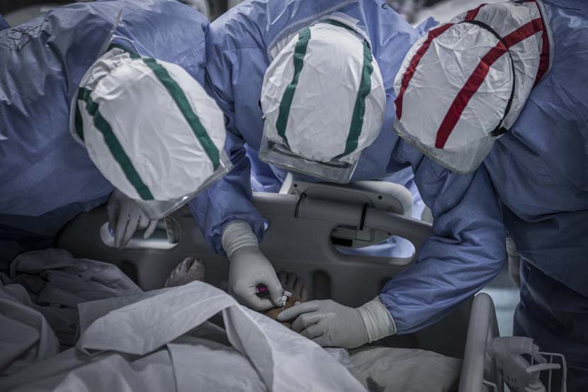 Three medical workers examine the arteries in a patient’s foot in the Wuhan Pulmonary Hospital ICU, Hubei province, March 13, 2020. Sun Zhan for Sixth Tone
