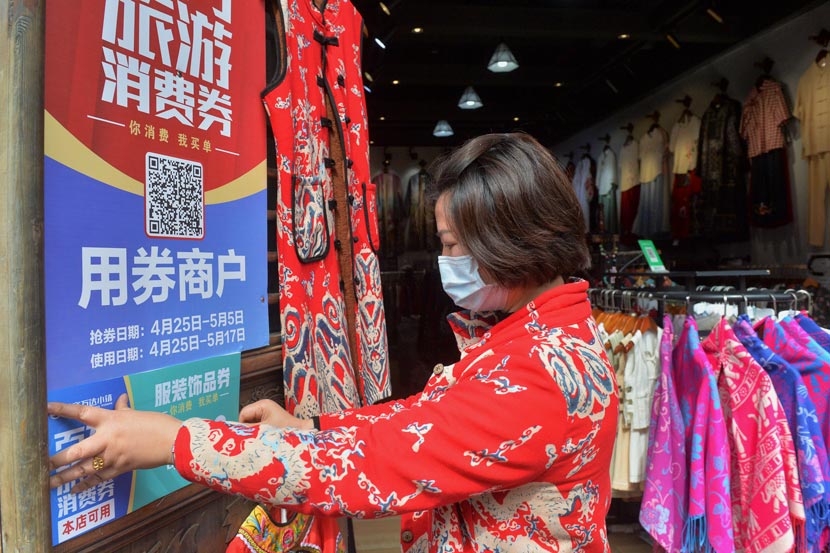 A clothing store owner hangs up a sign encouraging customers to use “consumption coupons” at a tourist attraction in Danzhai County, Guizhou province, April 25, 2020. Qiao Qiming/People Visual