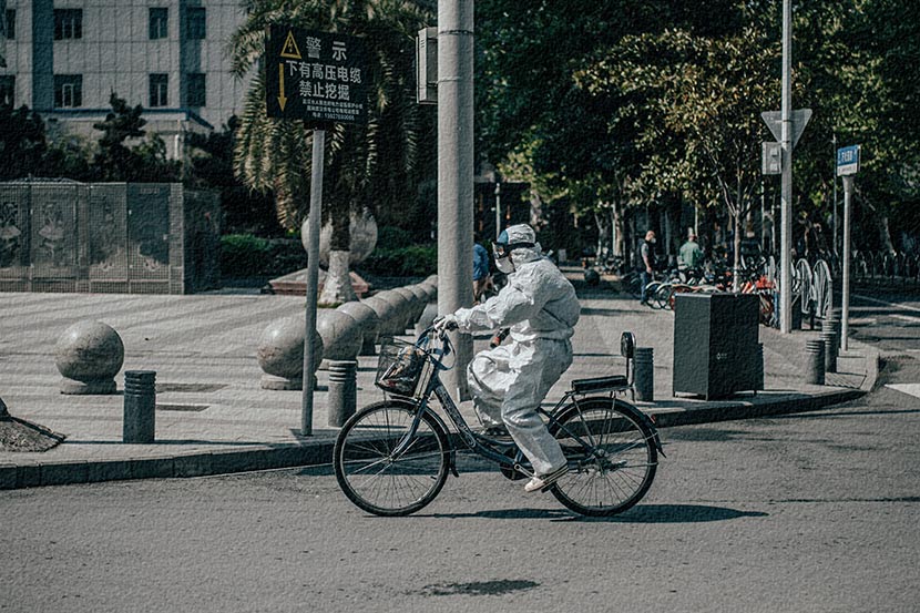 A resident in a protective suit bikes past Wuhan Union Hospital in Hubei province, April 12, 2020. Xia JIncan/People Visual