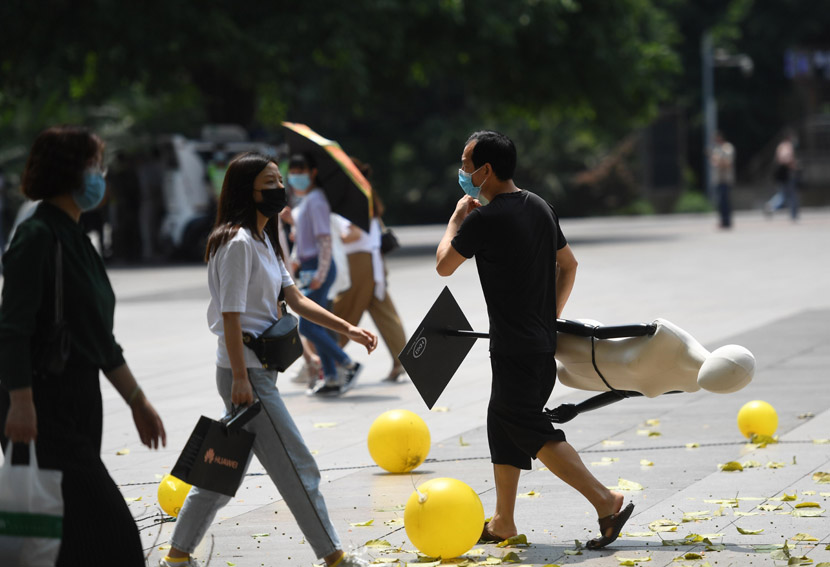 A man carrying a mannequin crosses a street in Chongqing, May 6, 2020. Chen Chao/CNS/People Visual