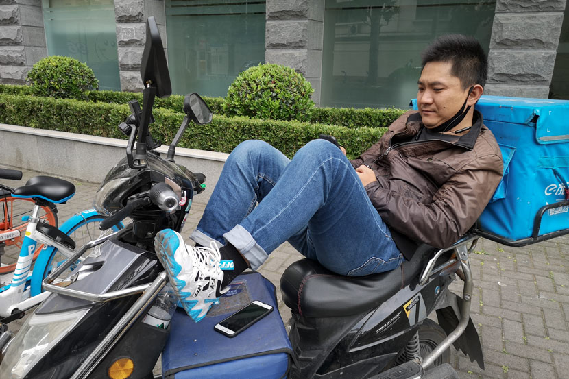 A delivery driver surnamed Jia looks at his phone during his downtime, Shanghai, May 14, 2020, Kenrick Davis/Sixth Tone