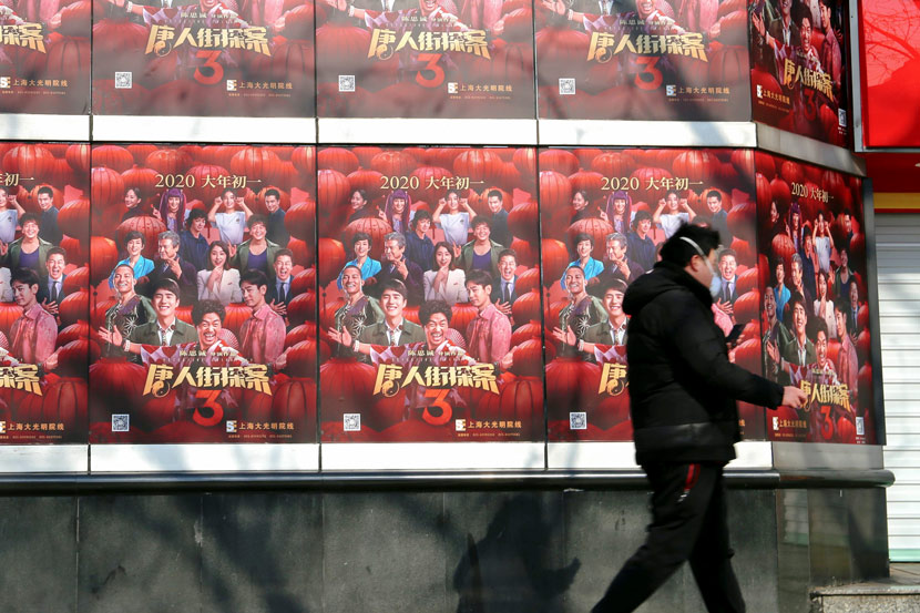 A man walks past a wall plastered with film posters outside a movie theater in Shanghai, Feb. 24, 2020. Chen Yuyu/People Visual