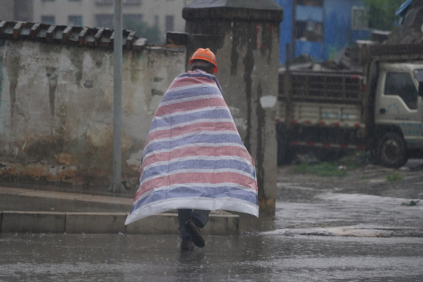 A migrant worker wraps himself in a plastic sheet on a rainy day in Kunming, Yunnan province, June 18, 2020. Liu Ranyang/CNS/People Visual