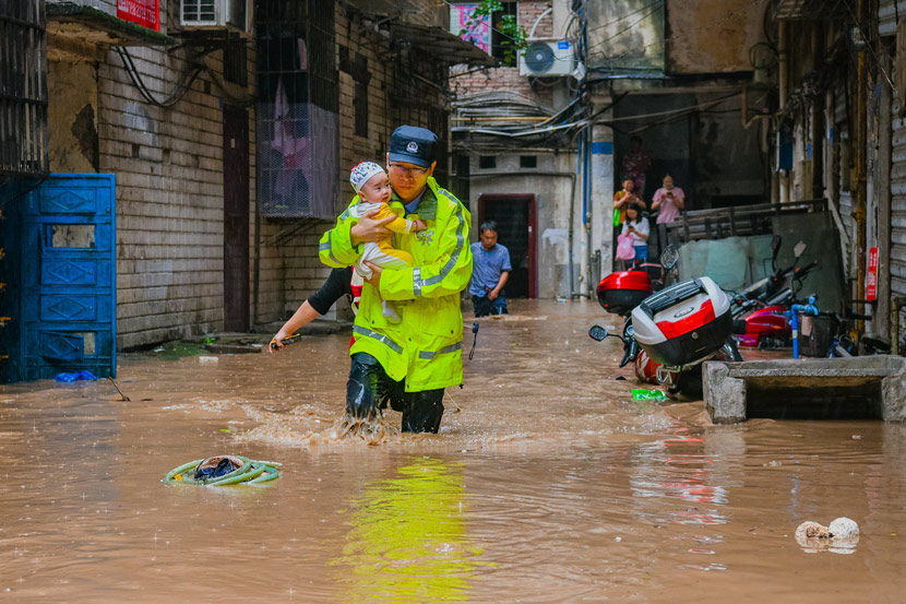 A police officer rescues a baby from a flooded neighborhood in Qijiang District, Chongqing, June 22, 2020. Chen Xingyu/People Visual