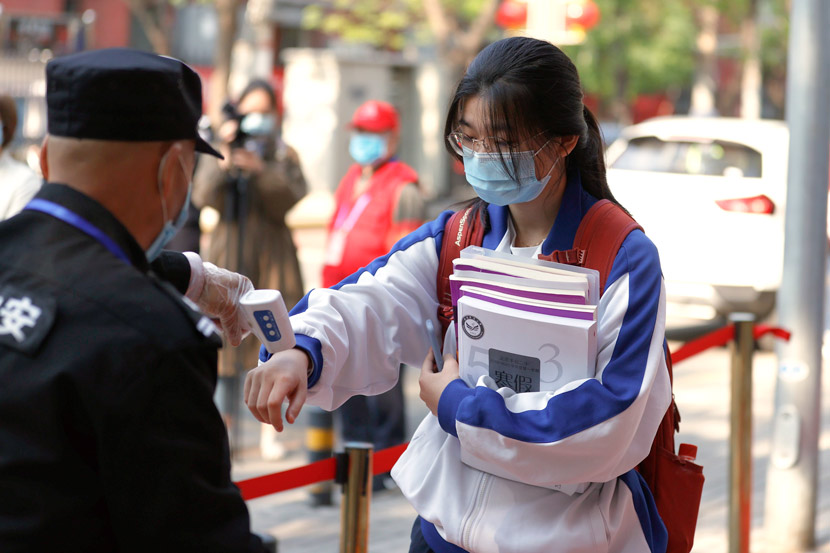 A security guard checks the body temperature of a student at the entrance to a high school in Beijing, April 27, 2020. It was the first day senior high school students returned to school following the COVID-19 outbreak. Fu Tian/CNS/People Visual