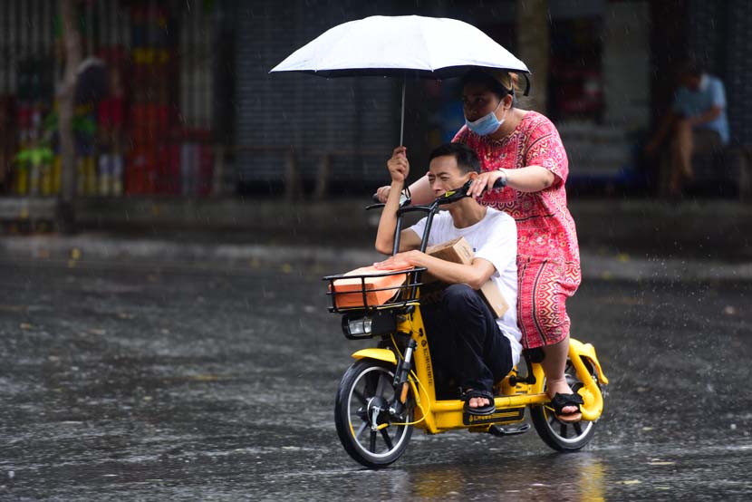 A man and a woman ride on an electric bike in the rain, Qionghai, Hainan province, June 14, 2020. People Visual
