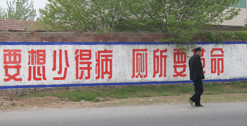 A villager walks past a slogan, reading, “If you want to get sick less, then we need a toilet revolution,” in Yucheng County, Henan province, April 23, 2010. IC