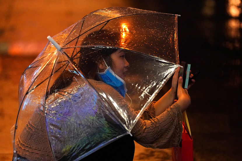 A woman juggles phone, umbrella, and mask on a rainy day in Beijing, Aug. 12, 2020. Tingshu Wang/People Visual