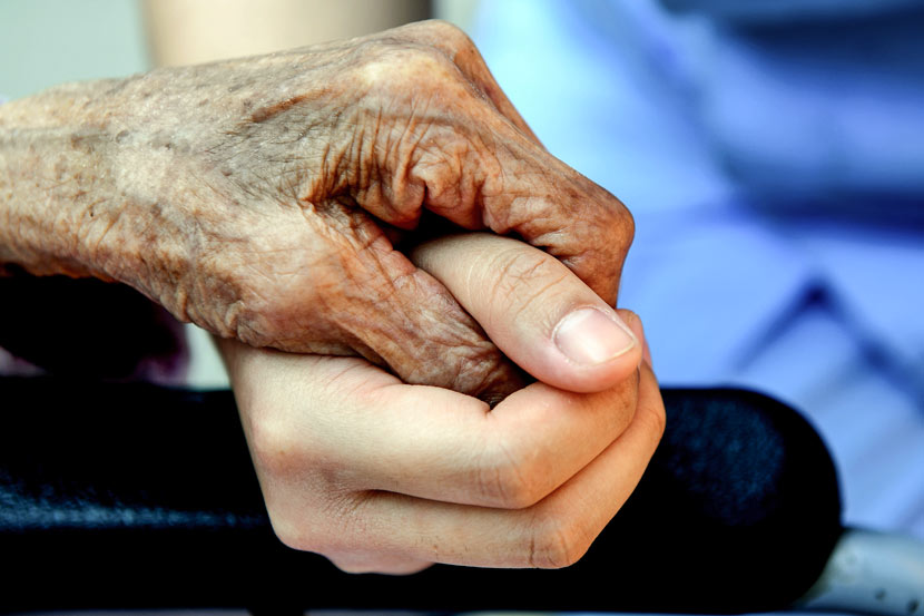An elderly woman holds a caretaker’s hand in Zhengzhou, Henan province, Sept. 21, 2016. Sha Lang/VCG