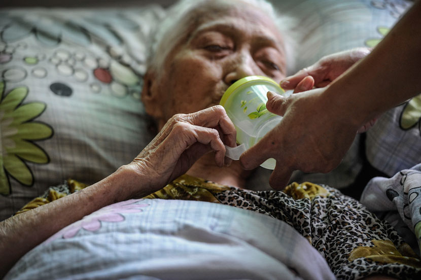 An elderly woman drinks from a cup with the help of a staff member at a nursing home in Zhongshan, Guangdong province, Oct. 9, 2013. Ye Zhiwen/VCG