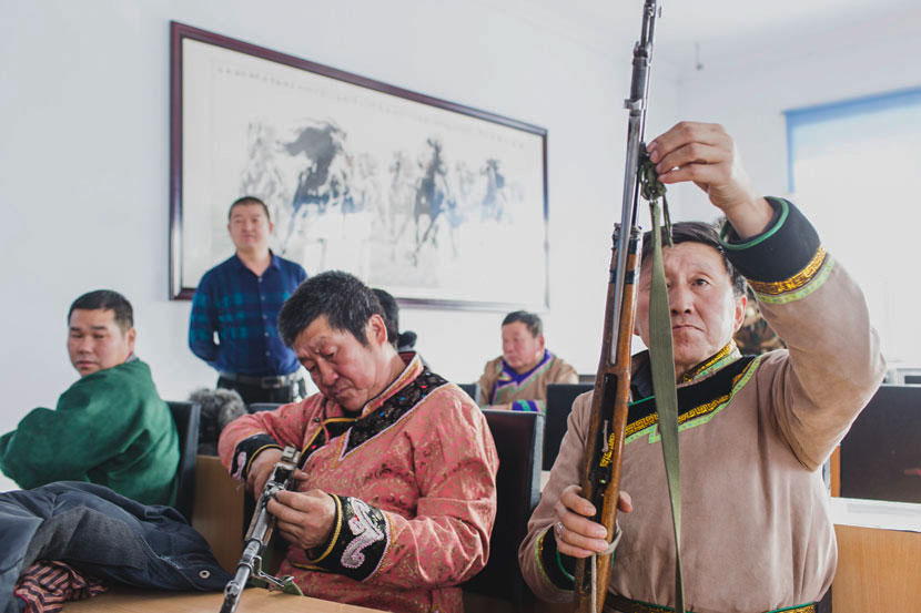 Hunters check their rifles in the meeting room of the local government in Xinsheng Township, Heihe, Heilongjiang province, Nov. 22, 2016. Zhou Pinglang/Sixth Tone