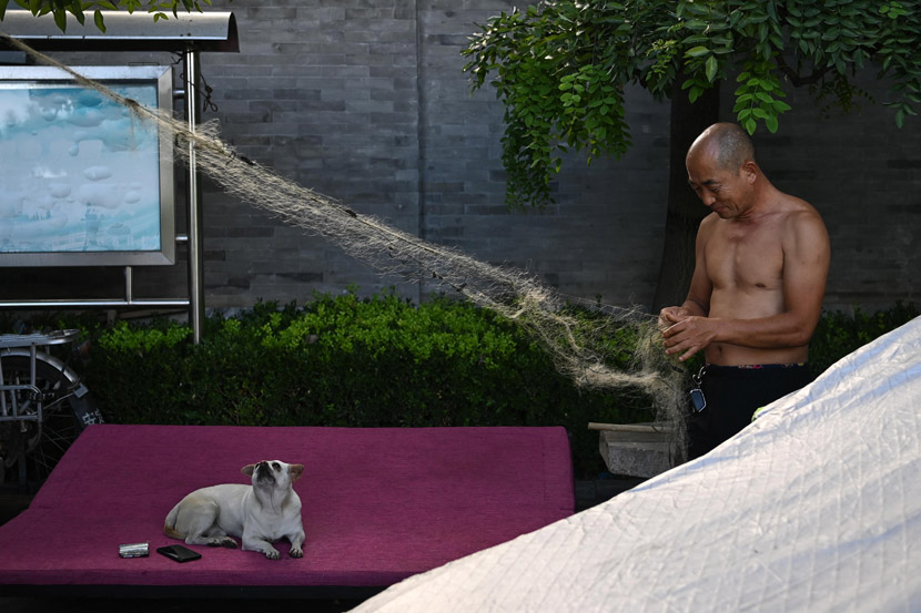 A resident repairs his fishing net while his pet dog watches in Beijing, Aug. 27, 2020. Cui Nan/CNS/People Visual