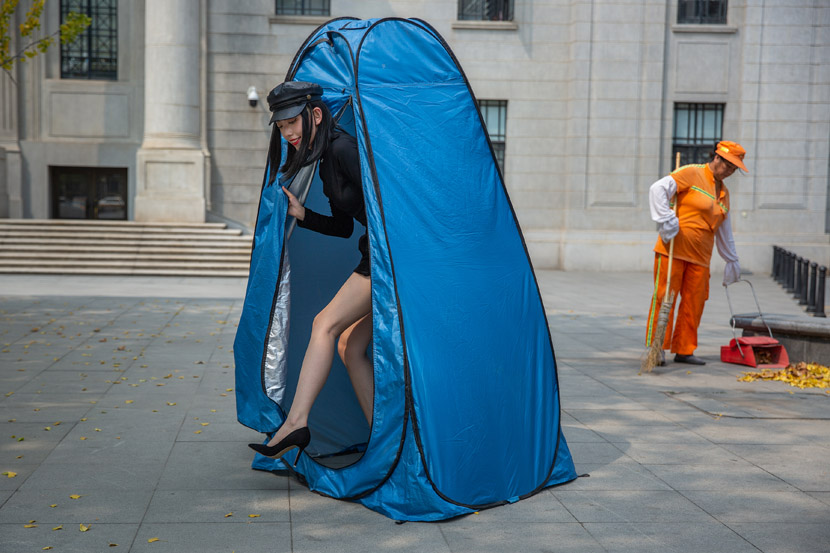 A model walks out of a changing tent, while a street cleaner sweeps in Wuhan, Hubei province, Sept. 8, 2020. Chen Zhongqiu/People Visual
