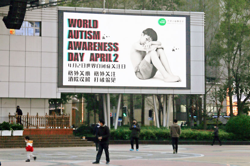 People walk past a poster promoting public awareness of autism, in Shanghai, April 1, 2020. People Visual