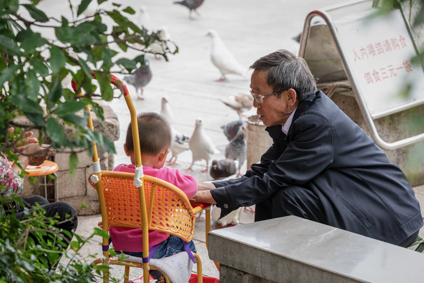 An elderly resident takes care of a child at a park in Qujing, Yunnan province, May 31, 2018. Wan Huizhou/People Visual