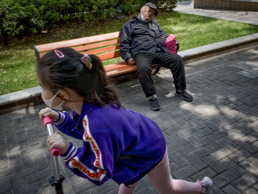 A girl plays on a scooter, while an elderly man takes a nap on a bench, in Shanghai, April 29, 2020. Zhang Yan/People Visual