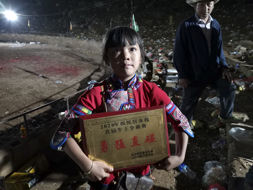 A girl in traditional Sani Yi dress dispays a plaque honoring the owner of the event’s best “charging bull” after a bullfight event in Shilin Yi Autonomous County, Yunnan province, October 2020. Kenrick Davis/Sixth Tone