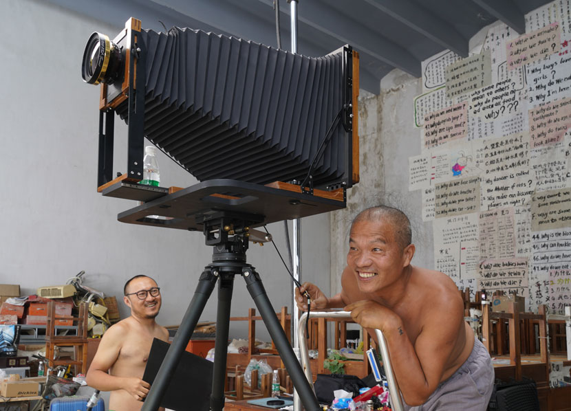 Wang Qingsong (right) at work during the creation of “Question A Brick Wall,” Beijing, June 2020. His tattoo can be seen on his left wrist. Courtesy of Wang Qingsong