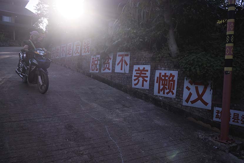 A villager rides a motorbike past a slogan promoting China's poverty alleviation campaign in Hebian Village, Yunnan province, Nov. 1, 2020. Wu Huiyuan/Sixth Tone