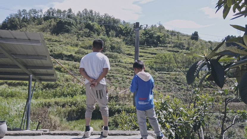 2020 年 9 月，王小平和他的儿子站在他们的山腰屋外，在重庆。 何凯为第六声