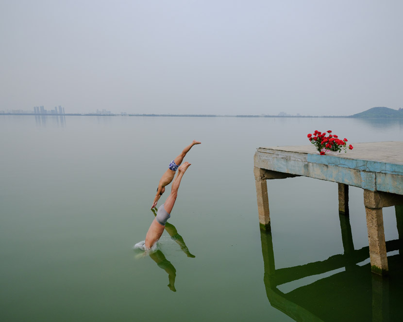 Two men jump into the East Lake, a popular site for diving enthusiasts in Wuhan, Hubei province, April 8, 2020. The flowers were left there by a man who had proposed to a woman on the pier. Shi Yangkun/Sixth Tone