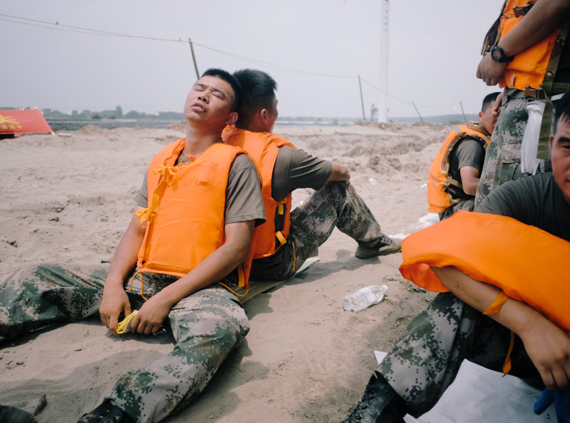 Two soldiers rest back-to-back during their shift reinforcing the dike in Jiangzhou County, Jiangxi province, July 16, 2020. Wu Huiyuan/Sixth Tone