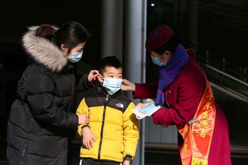 A volunteer helps a boy wear his mask properly at Chongqing North Railway Station, Jan. 28, 2021. People Visual