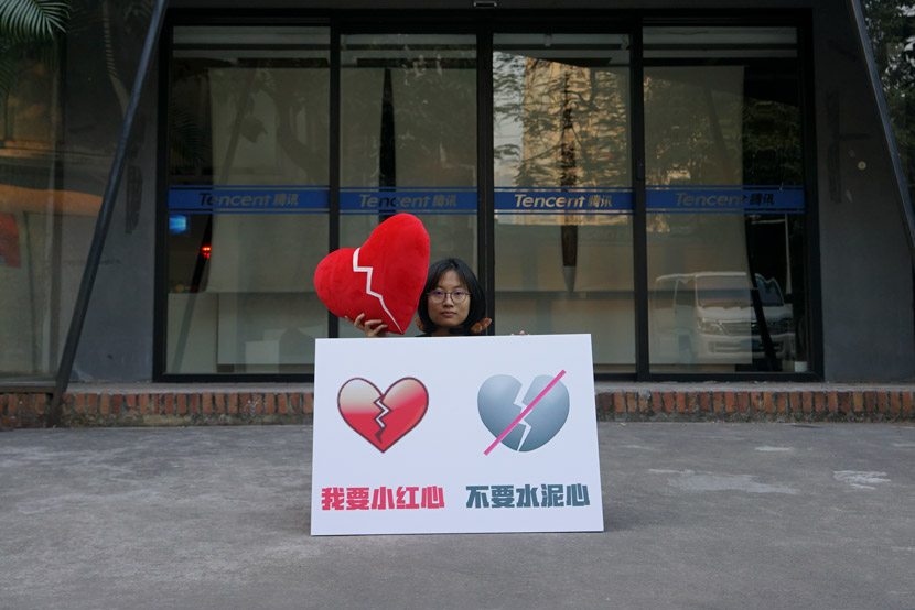 An artist holding a poster showing old (left) and new emojis poses for a photo in front of WeChat’s headquarters in Guangzhou, Guangdong province, Jan. 30, 2021. Courtesy of Wang Huadong