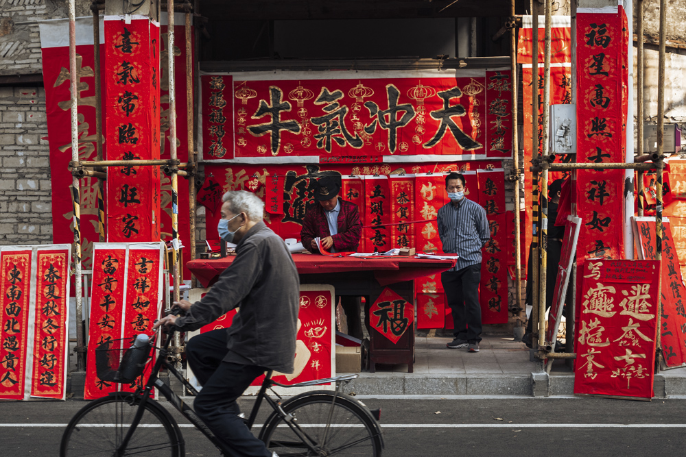 An elderly man rides past a booth selling spring couplets in Foshan, Guangdong province, Feb. 6, 2021. Long Yilin/People Visual